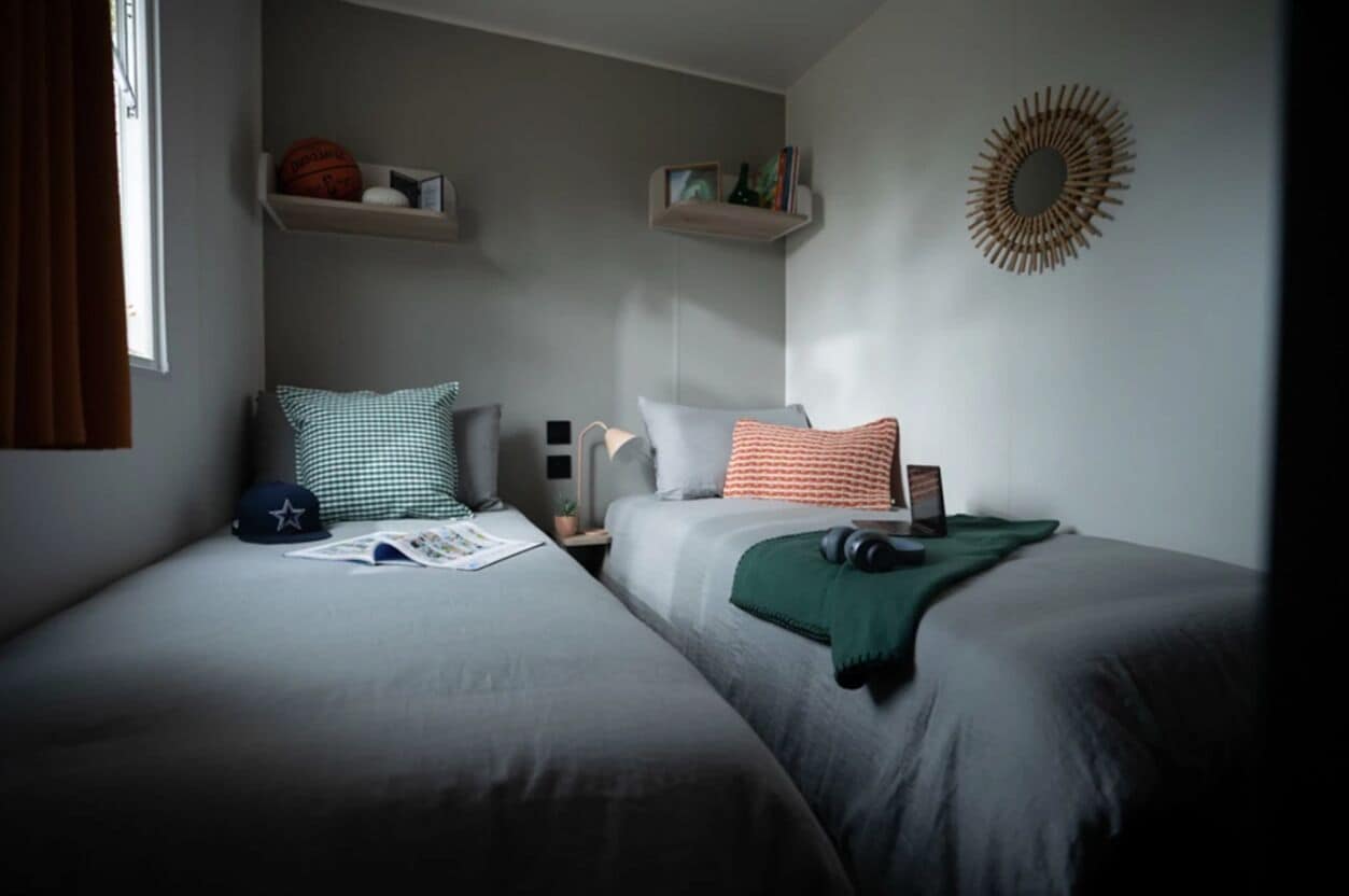 A bedroom with two beds, a window with curtains, shelves with books and a basketball, and a wall decoration.