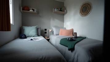 A bedroom with two beds, a window with curtains, shelves with books and a basketball, and a wall decoration.