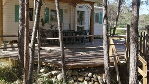 A wooden deck with outdoor furniture, a covered area with a door labeled "TRV", and a white mobile home with green shutters. - Résidence Santa (Ghisonaccia)