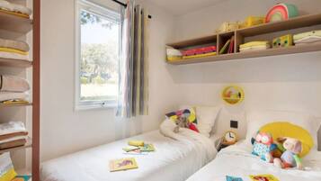 Un dormitorio con dos camas individuales, una ventana con cortinas, un estante con juguetes infantiles y un reloj de pared.