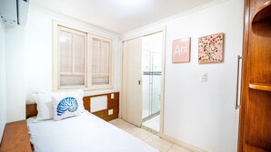 A bedroom with a bed, a wooden headboard, a window with blinds, a door leading to a balcony, and two wall-mounted pictures.