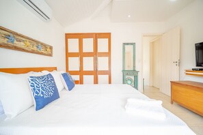 Quarto de hotel com uma cama grande, um guarda-roupa de madeira, uma televisão e um espelho.