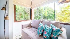 A modern interior with a sofa and large windows offering a view of greenery. - Bz86 Casa centro 600m da rua das pedras (Buzios)