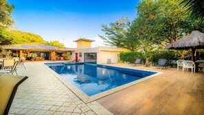 Piscina com espreguiçadeiras e área de estar coberta.