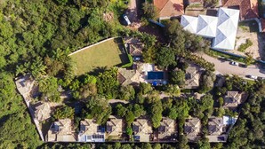 Vista aérea de un resort con varias cabañas, una amplia piscina central y exuberante vegetación circundante.