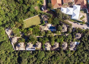 Vista aérea de um resort com várias acomodações tipo bangalô, uma piscina grande no centro e vegetação exuberante ao redor.