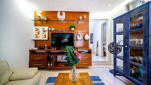A living room with a wooden entertainment unit, a TV, a sofa, a coffee table with a vase, and a cabinet with glass doors.