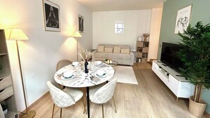A modern living room with a round dining table, two white cushioned chairs, a sofa, a TV, and a potted plant. - Apartment - Arc de Triomphe - 4 people (Paris)