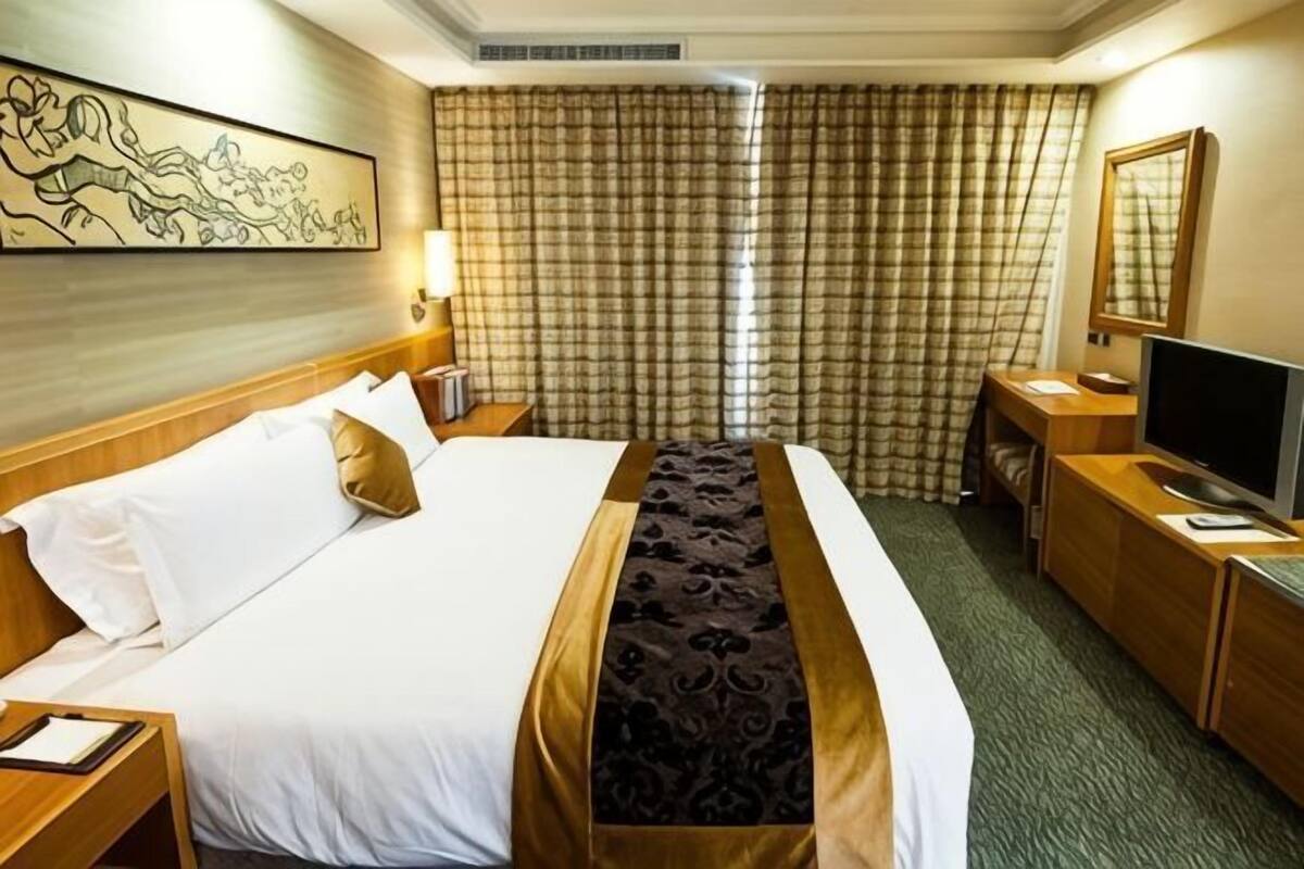 Une chambre d’hôtel avec un grand lit, un bureau avec une télévision, une lampe de bureau et une fenêtre avec des rideaux.