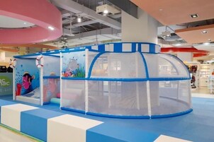 Zona de juegos infantiles con una estructura de juegos azul y blanca, rodeada por una red de seguridad.