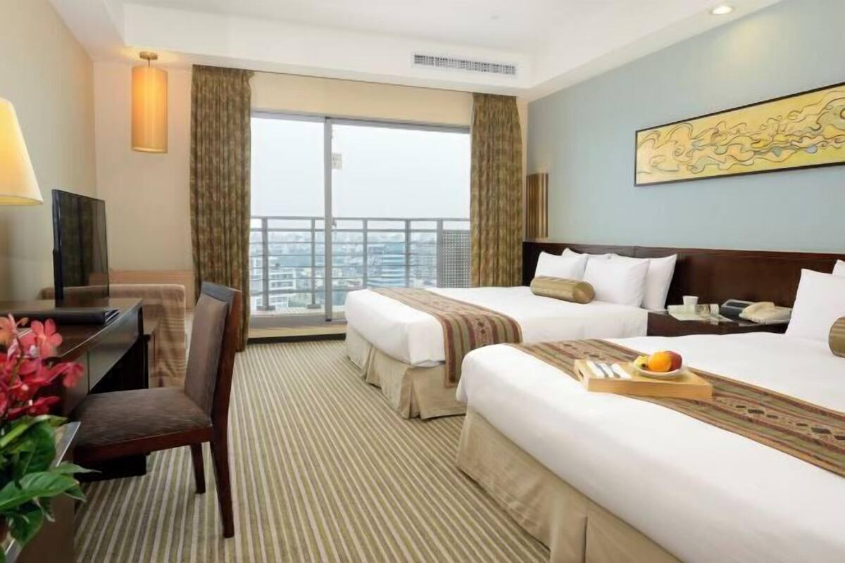 Une chambre d’hôtel avec deux lits, un bureau, une chaise, une télévision et un balcon offrant une vue sur la ville.