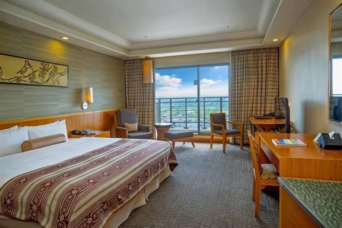 Une chambre d’hôtel avec un grand lit, un bureau, deux chaises, un balcon avec vue et un tableau au mur.