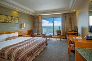 Une chambre d’hôtel avec un grand lit, un bureau, deux chaises, un balcon avec vue et un tableau au mur.