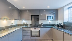 A modern kitchen with grey cabinets, a built-in oven, and a microwave. - 4-Bedroom Seafront House in Southend | Sea Views - Pass the Keys (Southend-on-Sea)