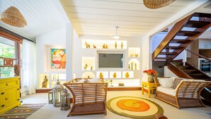 A spacious living room with a large TV, wicker furniture, and a staircase. - Bz87 Casa Churrasqueira 200m da Praia (Buzios)