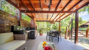 An outdoor patio with a wooden pergola, a wicker sofa, a dining table with chairs, and a small table with a vase of flowers. - Bz87 Casa Churrasqueira 200m da Praia (Buzios)