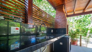 A modern kitchen with a black countertop, stainless steel sink, and a brick wall. - Bz87 Casa Churrasqueira 200m da Praia (Buzios)