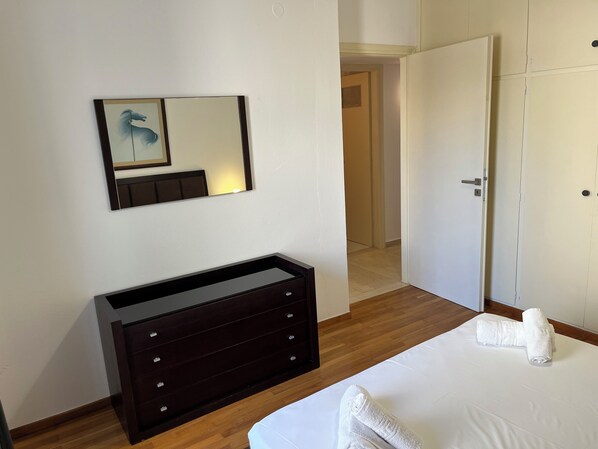 A hotel room with a large bed, a dark wooden dresser, a mirror with a horse painting, and a door leading to another room. - Beachfront Paradise (Rethymno)