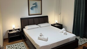 A neatly made bed with white linens and two rolled towels, a framed abstract painting above the headboard, and a modern light fixture hanging from the ceiling. - Beachfront Paradise (Rethymno)