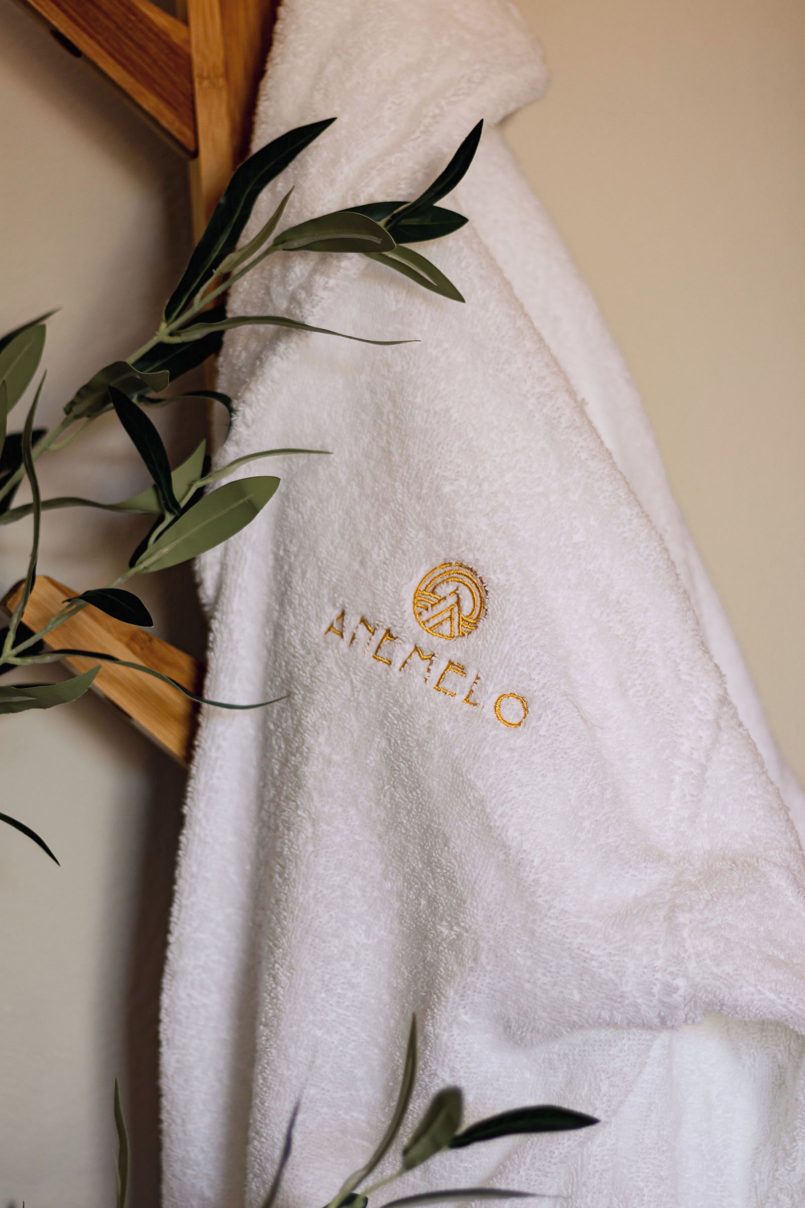 A white towel with embroidered text and a logo, hanging on a wooden surface.