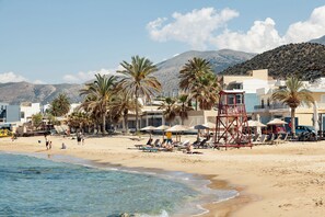 A beach with palm trees, beach chairs, umbrellas, and a lifeguard tower.