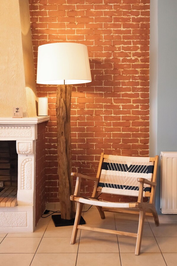 A room with a brick wall, a white fireplace, a wooden floor lamp, and a woven chair.
