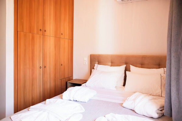 A neatly made bed with white linens and pillows, a wooden wardrobe, and a small bedside table.