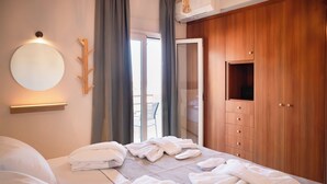 A hotel room with a bed, a wooden wardrobe, a round mirror, and a balcony.