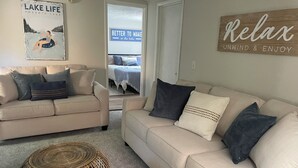 Un salón con dos sofás color beige, un reposapiés de mimbre y una pared con un letrero que dice "Relax."