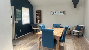 Un comedor con una mesa de madera y sillas tapizadas en azul, una estantería y un letrero que dice "SUN AND FUN".