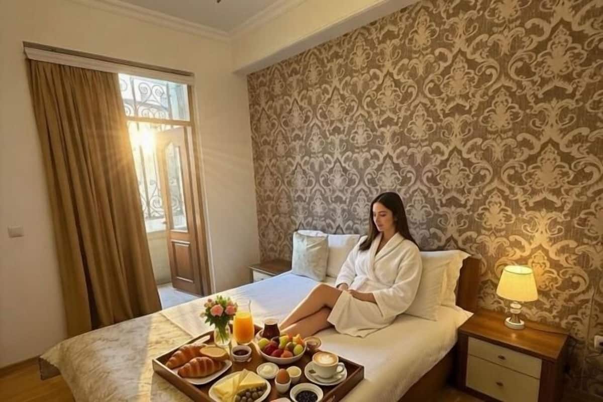Ein Hotelzimmer mit einem Bett, einem Frühstücksbrett, einem Nachttisch mit Lampe und einer Wand mit Muster.
