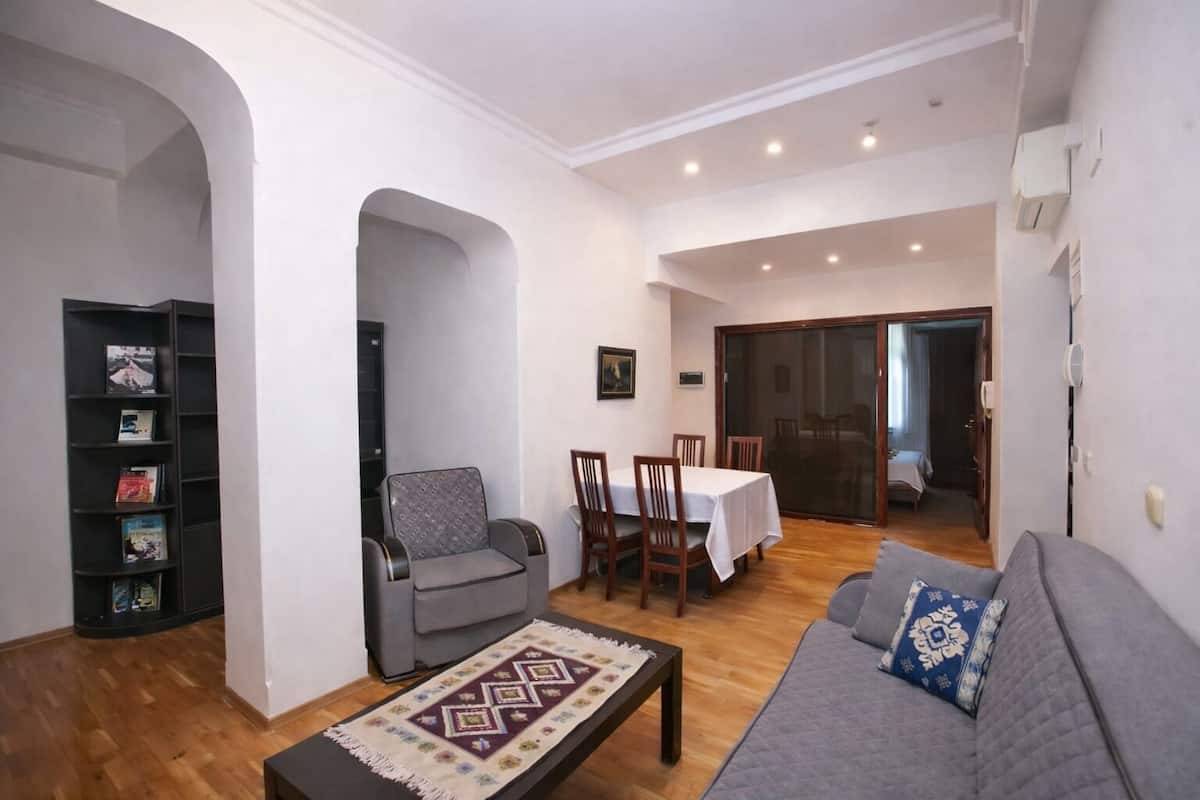 Ein Wohnzimmer mit einer Couch, einem Couchtisch, einem Bücherregal und einem Essbereich mit Stühlen und einem Tisch.
