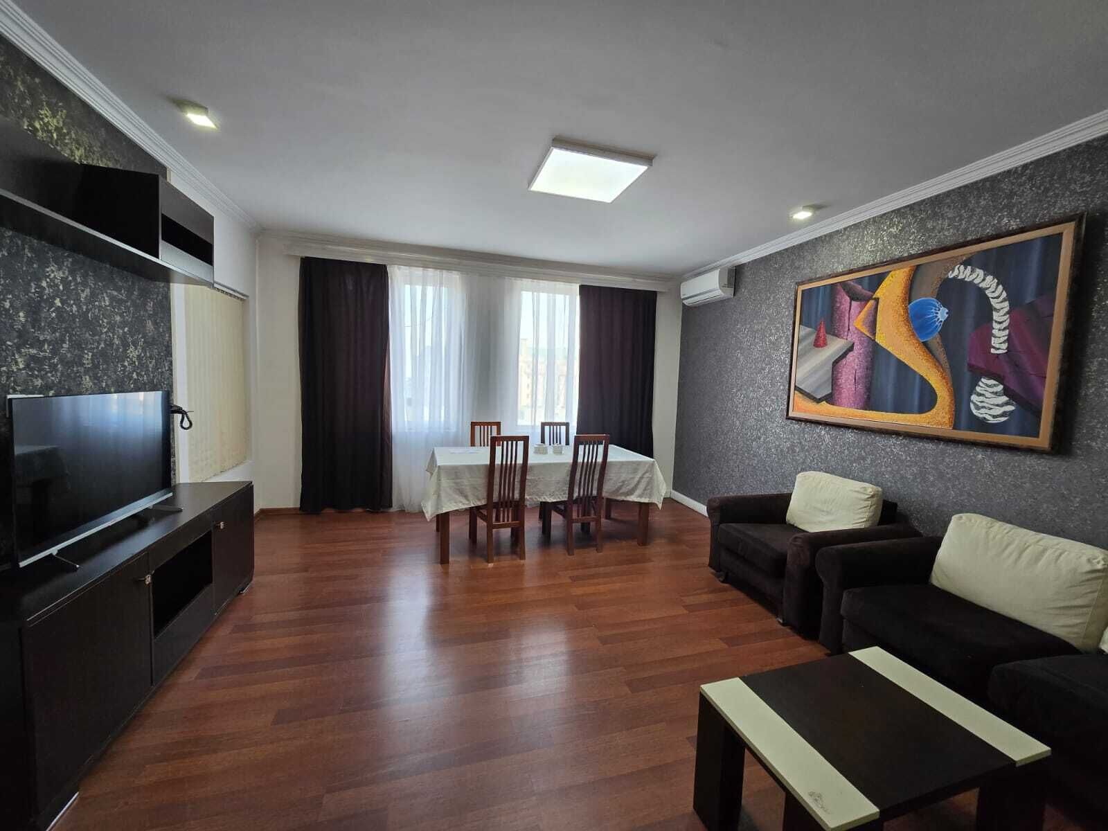 Ein Wohnzimmer mit Fernseher, Esstisch mit Stühlen, einer Couch und einem Gemälde an der Wand.