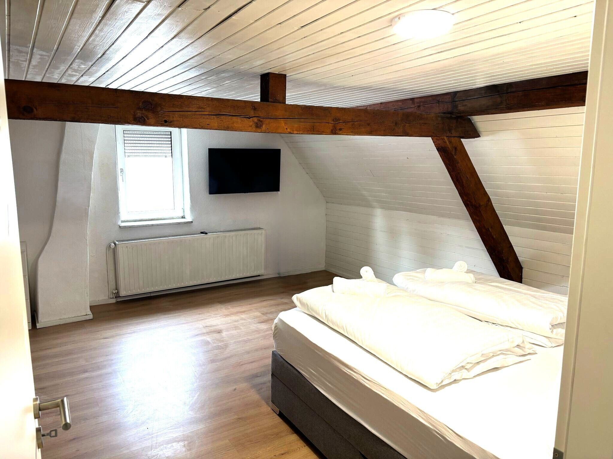 A bedroom with a sloped ceiling, a bed, a radiator, and a window.