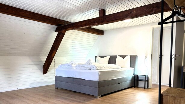 Ein Schlafzimmer mit einem Bett, Holzboden, weißen Wänden und einer geneigten Decke.