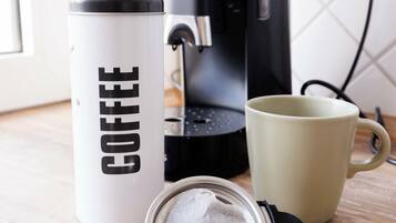 A coffee maker, a mug, a coffee container, and coffee pods on a wooden surface.