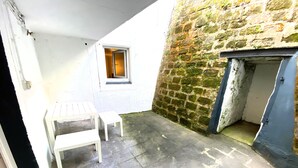 Ein kleiner, abgeschlossener Innenhof mit einer Steinmauer, einem Holztisch und einer Tür.
