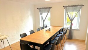 Ein Konferenzraum mit einem langen Holztisch, schwarzen Stühlen und zwei Fenstern mit Vorhängen.