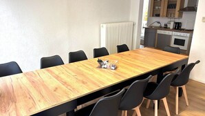 Ein Essbereich mit einem Holztisch und schwarzen Stühlen, im Hintergrund eine Küche und eine Heizung an der Wand.
