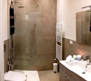 A modern bathroom with a glass-enclosed shower, a white toilet, a sink with a mirror, and a towel rack. - Renovated, located in the city center, and just a stone's throw from the ocean, with parking available (Livorno)