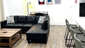Ein modernes Wohnzimmer mit einer schwarzen Ledersofa, einem Holztisch und einer Küchenzeile mit Barhocker.