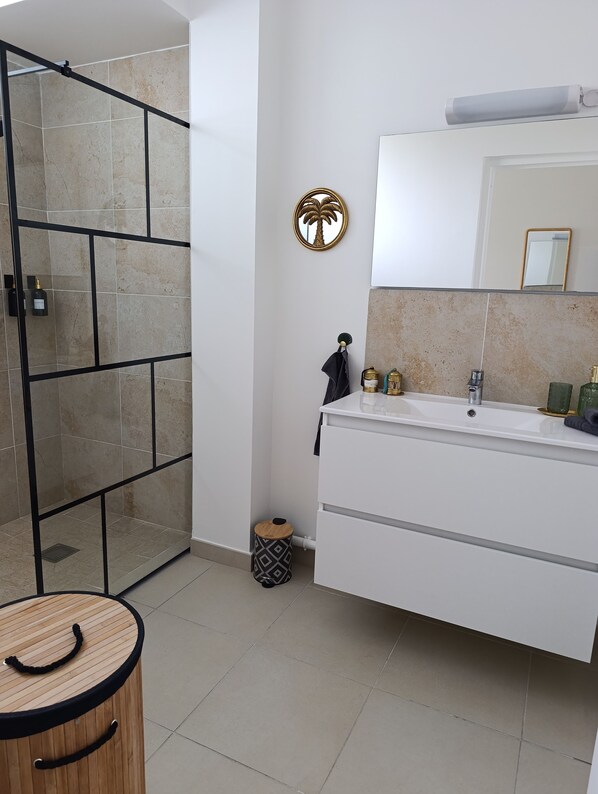 A modern bathroom with a glass shower enclosure, a white vanity with a mirror, and a small trash bin.