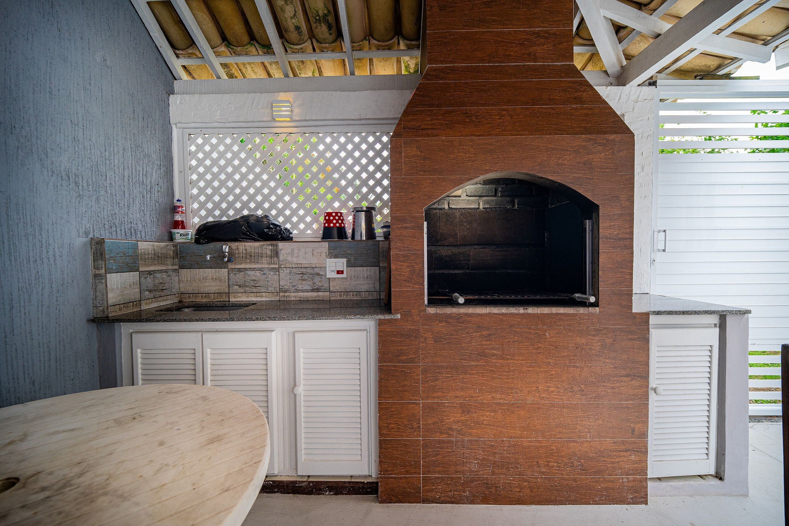 An outdoor kitchen with a brick oven, a wooden table, and a white fence.