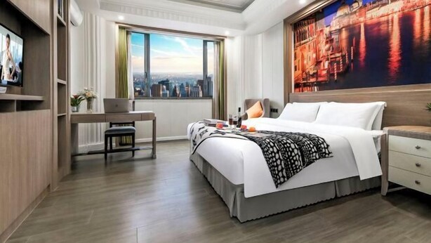 A hotel room with a bed, a desk, a chair, a TV, and a large window with a city view. - Xiyue Holiday Hotel (Chongqing Liangping New City Branch) (Chongqing)