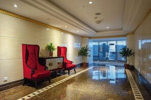 Un vestíbulo de hotel con piso de mármol pulido, asientos tapizados en rojo y vista a través de un vidrio.