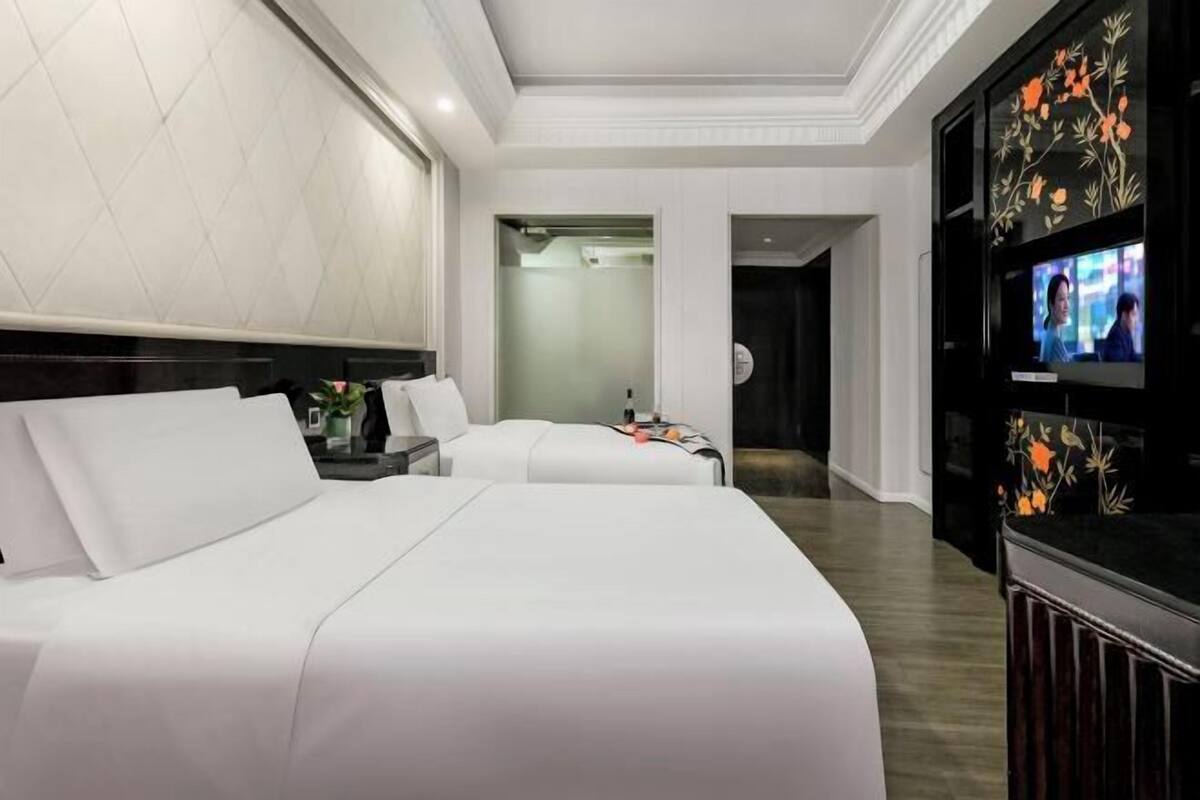 Een hotelkamer met twee bedden, een televisie en een badkamer zichtbaar door een glazen deur.