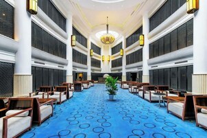 Un vestíbulo de hotel con alfombra azul, filas de asientos y un candelabro.