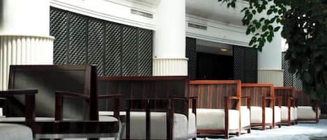 A row of wooden chairs and sofas arranged outside a building with a patterned facade.