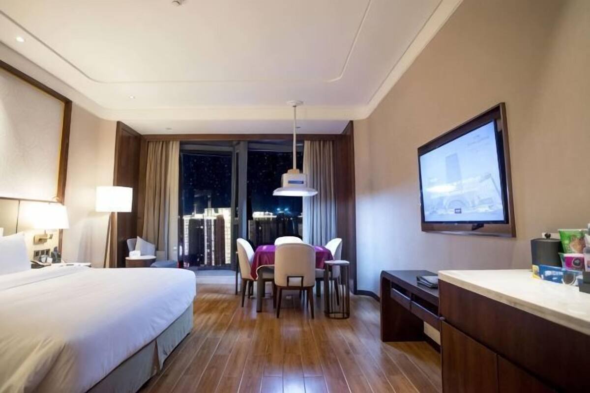 Hotelkamer met een bed, bureau, stoel, televisie en uitzicht op de stad 's nachts.
