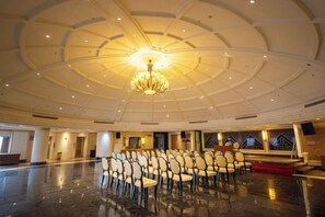Un gran salón con techo alto, una araña de cristal, asientos dispuestos y un escenario.